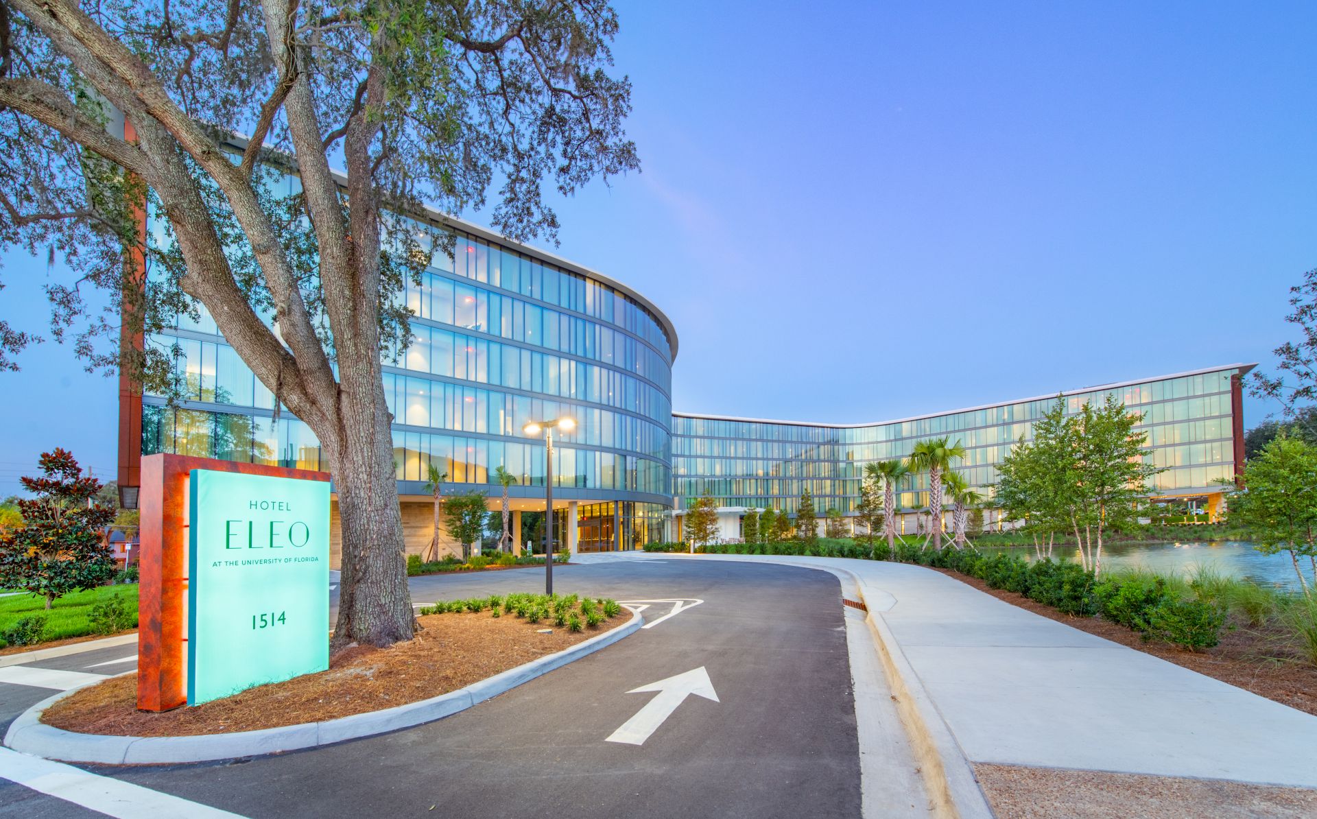 A modern glass building with a curved design, surrounded by greenery, and a sign labeled "LLEO" at the entrance.