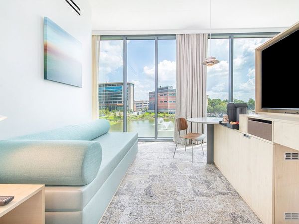 A modern, brightly lit room with a couch, table and chairs, large window with a cityscape view, TV, and minimalistic decor.