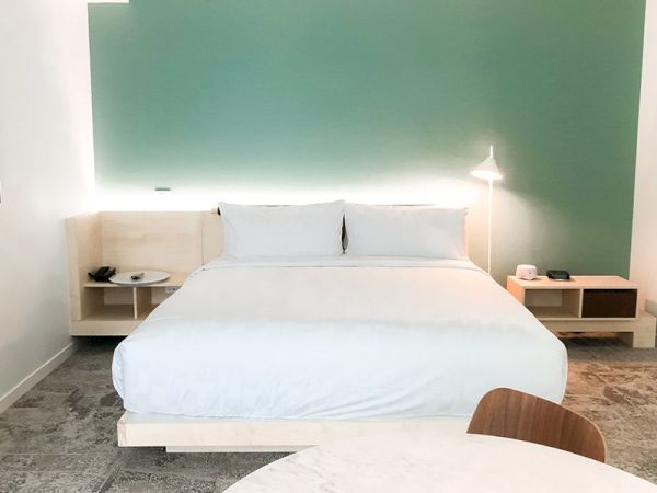 A modern bedroom with a neatly made bed with white linens, white pillows, green accent wall, and bedside tables with lamps and items on them.