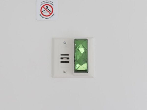 The image shows a wall-mounted button with a green light for guests with hearing impairments.