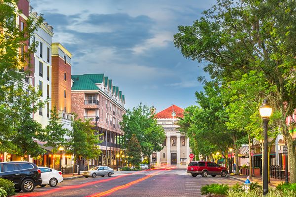 This image shows a quaint downtown street with parked cars, trees, and buildings, including a prominent structure with a red roof at the end.