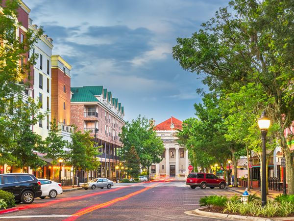 This image shows a quaint downtown street with parked cars, trees, and buildings, including a prominent structure with a red roof at the end.