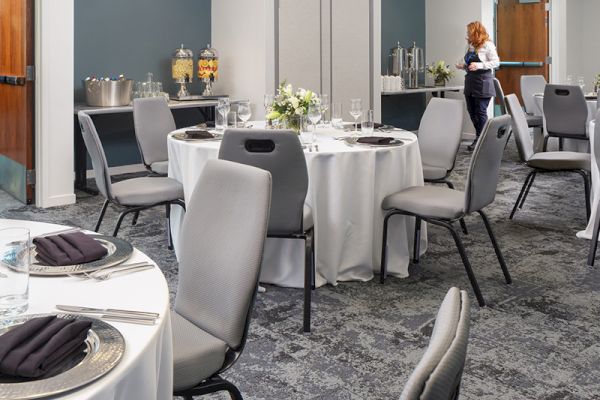 This image shows a set banquet room with round tables, chairs, decorative place settings, and a server preparing the space.