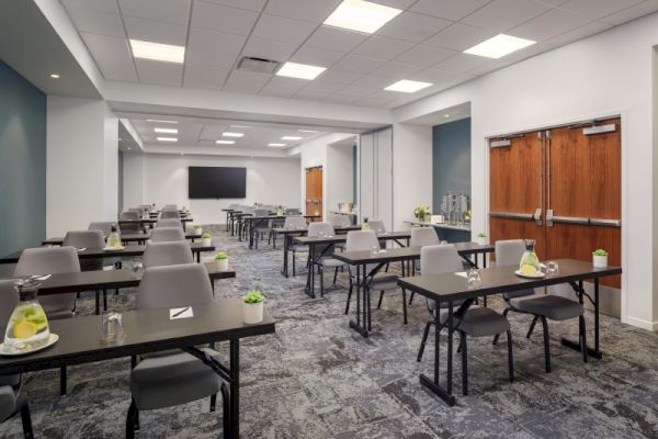 A modern conference room with rows of desks and chairs, a large TV screen at the front, and refreshments placed on the tables, ending the sentence.