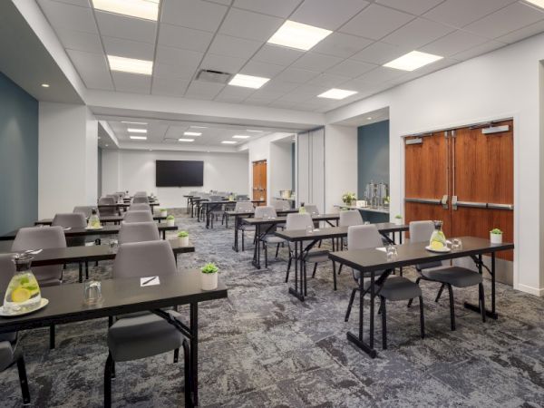 A modern conference room with rows of desks and chairs, a large TV screen at the front, and refreshments placed on the tables, ending the sentence.