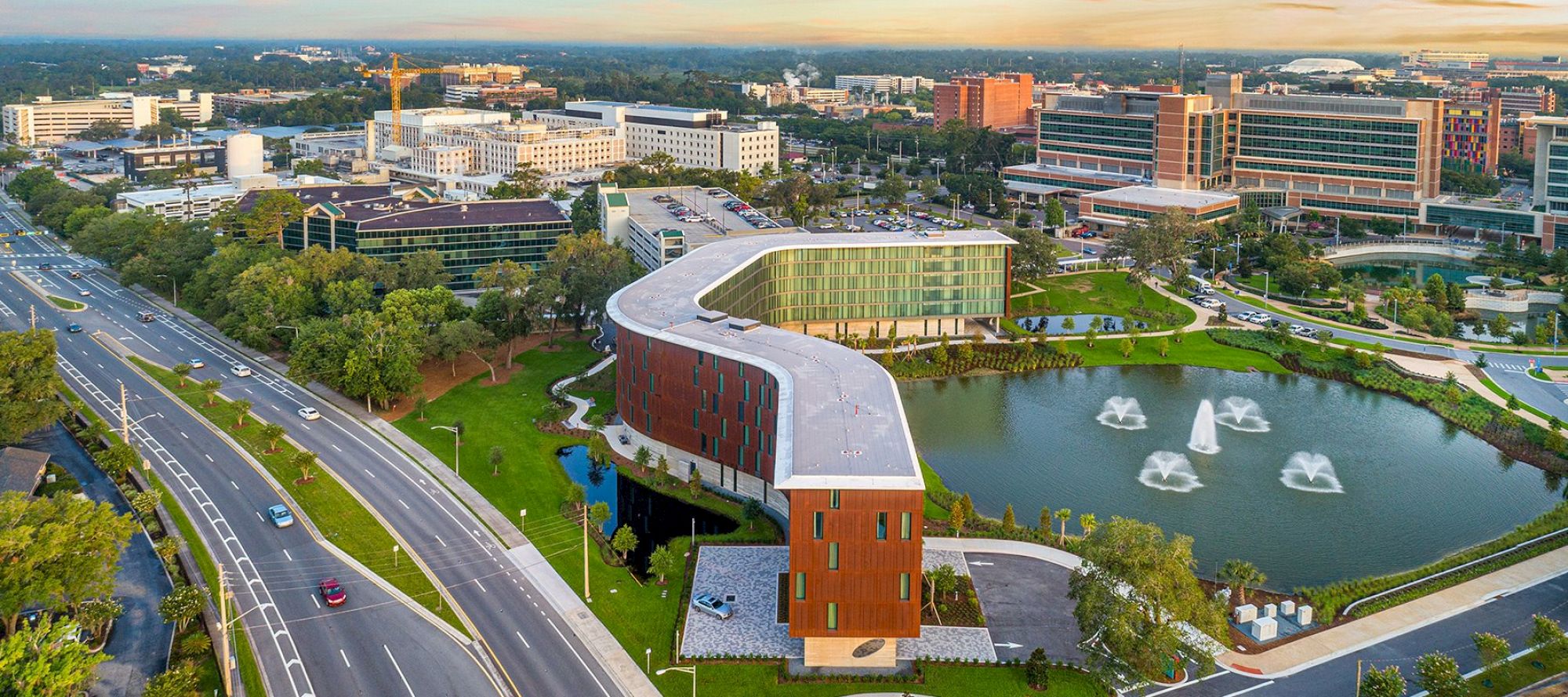 This image shows a modern architectural building near a pond with fountains, surrounded by roads and urban infrastructure.