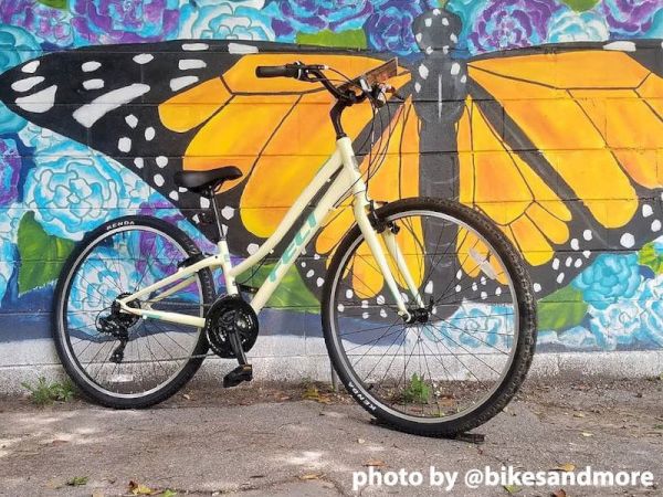 A bicycle is parked in front of a colorful mural featuring a large butterfly with vibrant wings and flowers. Photo by @bikesandmore.