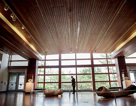 A person stands in a spacious, well-lit room with large windows and modern furniture, observing the surrounding environment.