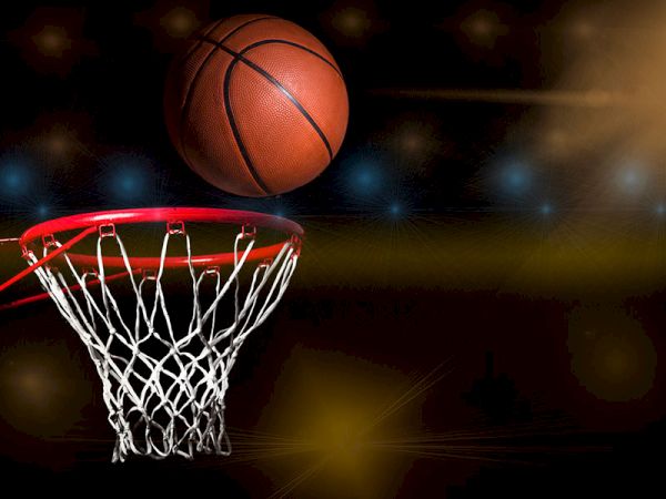 A basketball is captured in mid-air above a hoop, with a blurred background of lights and colors.