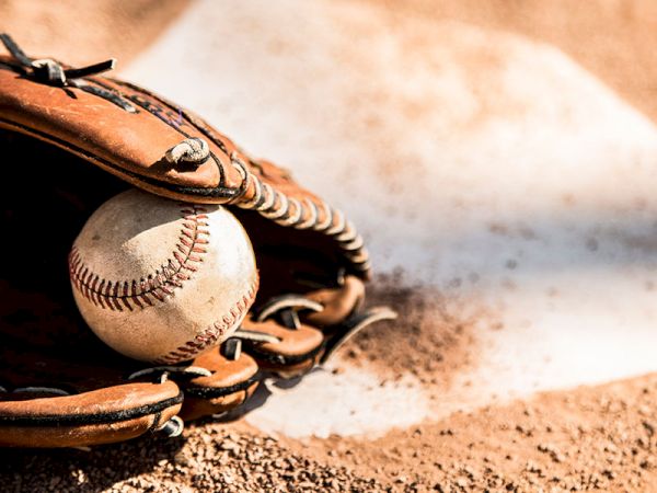 A baseball glove holding a baseball, placed on the ground near home plate on a baseball field, with some dirt visible.
