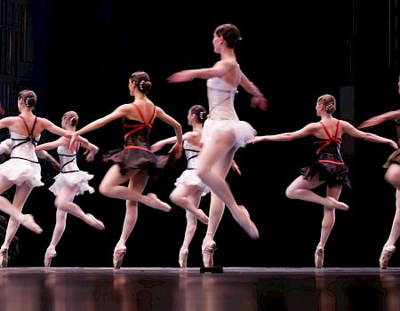 Ballet dancers in tutus are performing on stage, showcasing their grace and skills in a choreographed routine with elegant movements.