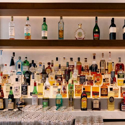 Shelves stocked with various liquor bottles and wine, with glasses and barware at the bottom, forming a detailed and organized bar setup.