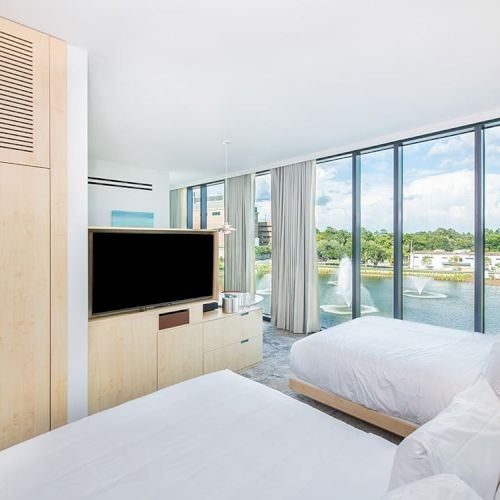 A modern hotel room with two beds, a flat-screen TV, large windows, and a scenic view outside.