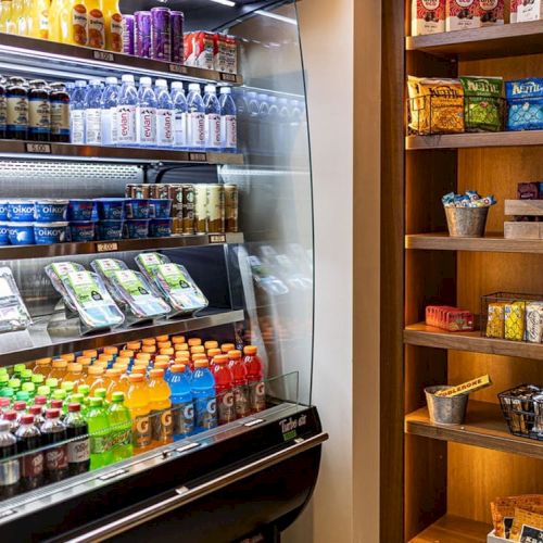 The image shows a refrigerated display with beverages and snacks, alongside shelves stocked with various packaged snacks and goods.