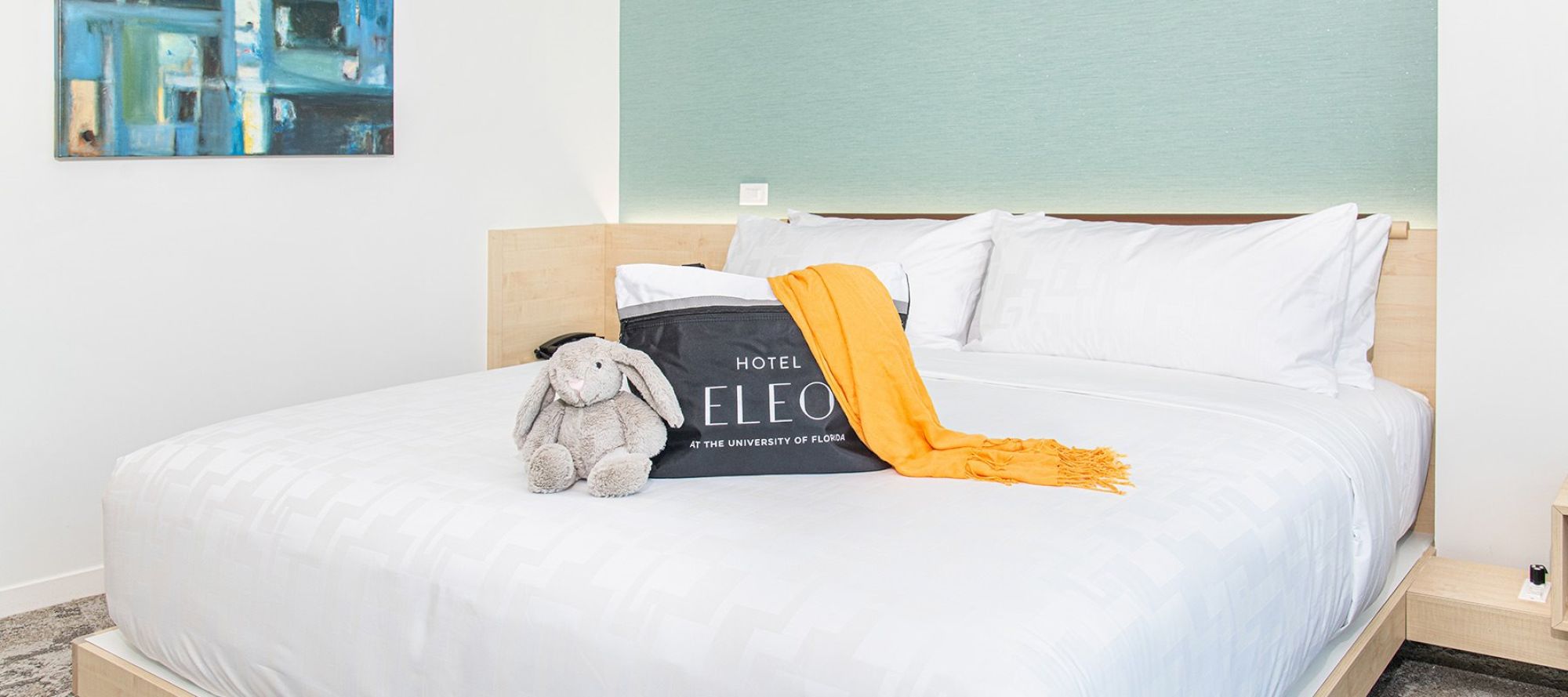 A neatly made bed with white linens, a stuffed bunny, a pillow sign that says 