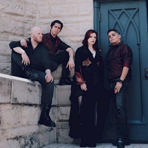 Four people pose in front of a stone wall and blue door, dressed in dark clothing.