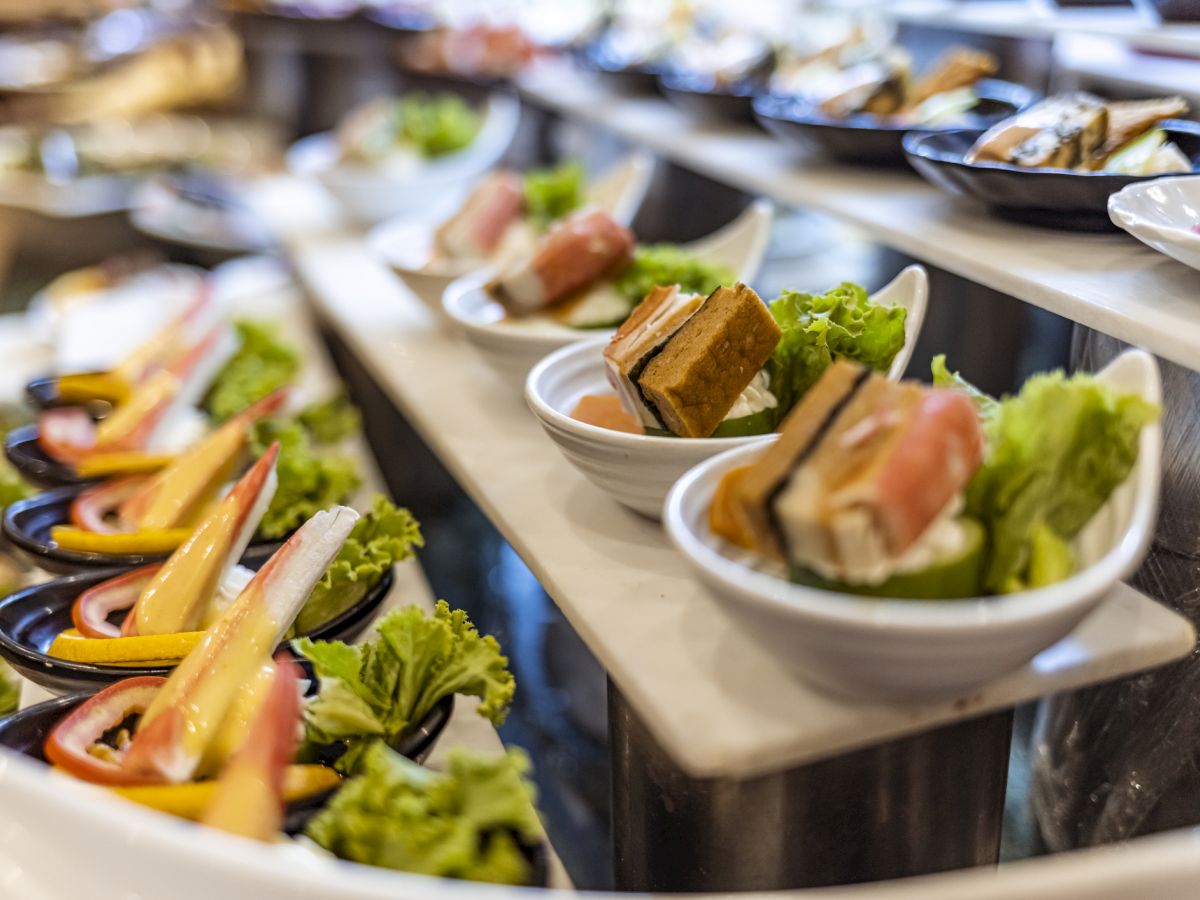 The image shows an assortment of small dishes on a multi-tiered display, featuring various appetizers, including sushi and salads.