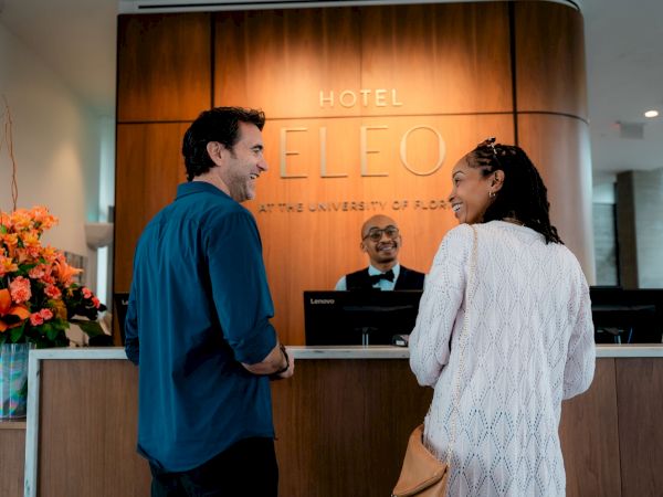 A man and woman are at a hotel reception desk, chatting with a receptionist.