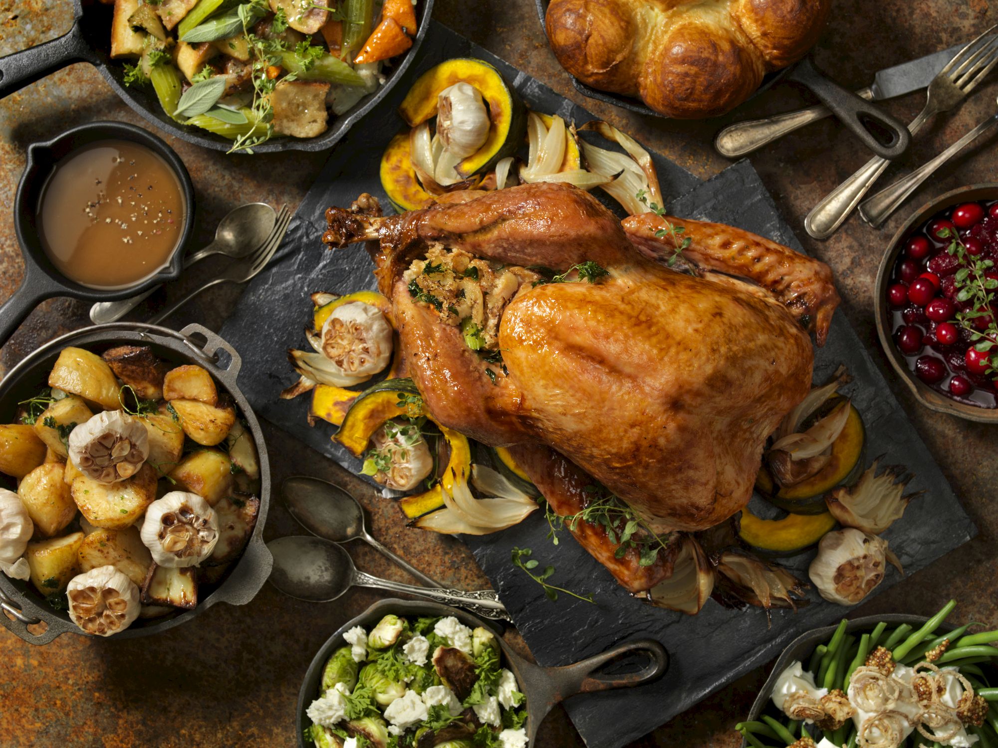 A Thanksgiving feast with roasted turkey, stuffing, potatoes, gravy, vegetables, cranberry sauce, and rolls on a table.