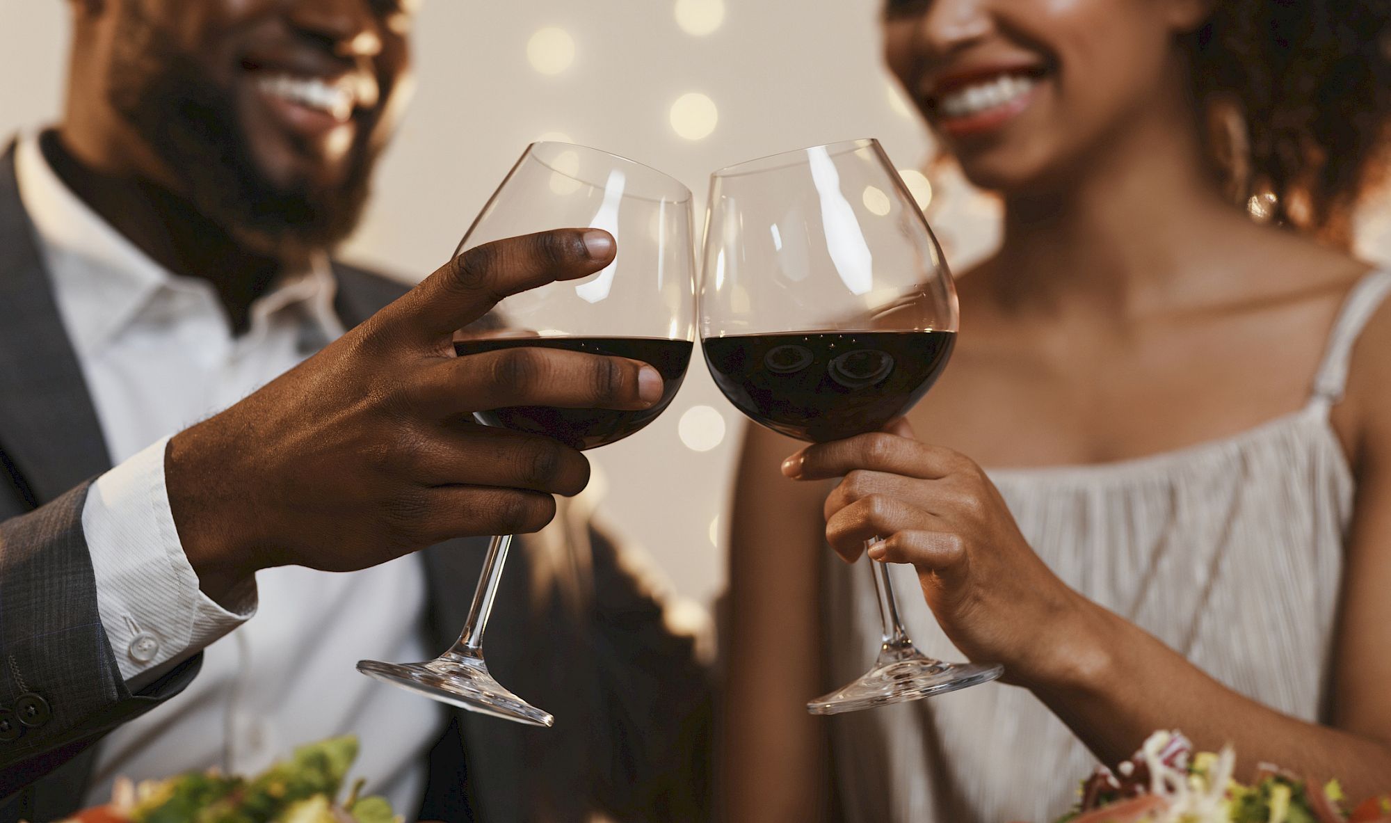 A couple is clinking wine glasses and smiling, enjoying a celebratory moment together.