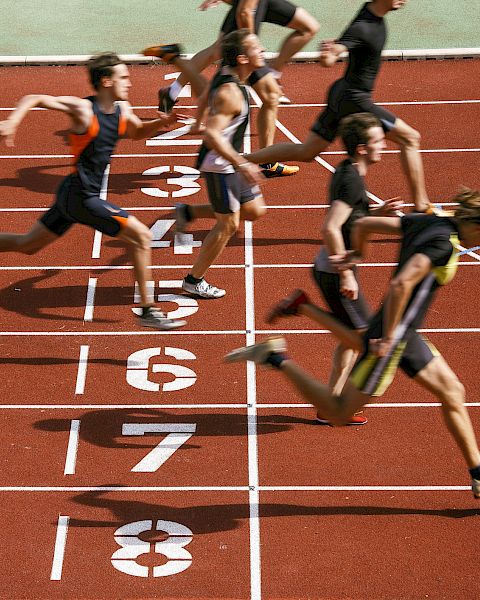 Runners cross the finish line on a track, captured in mid-stride at the end of a race.