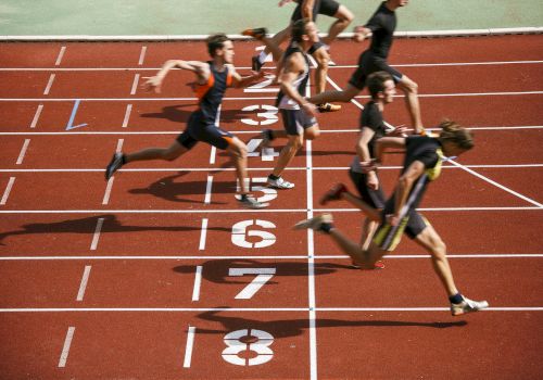 Runners cross the finish line on a track, captured in mid-stride at the end of a race.