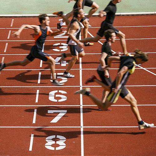 Runners cross the finish line on a track, captured in mid-stride at the end of a race.