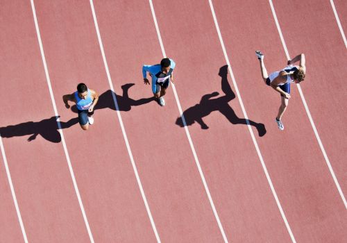 Three people are running on a track, casting long shadows on the surface, with one appearing to jump mid-stride.