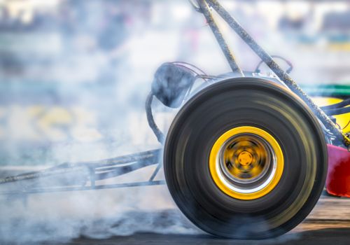 A close-up of a drag racing car's wheel, spinning and emitting smoke during a high-speed race, with a blurred background.