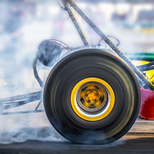 A close-up of a drag racing car's wheel, spinning and emitting smoke during a high-speed race, with a blurred background.