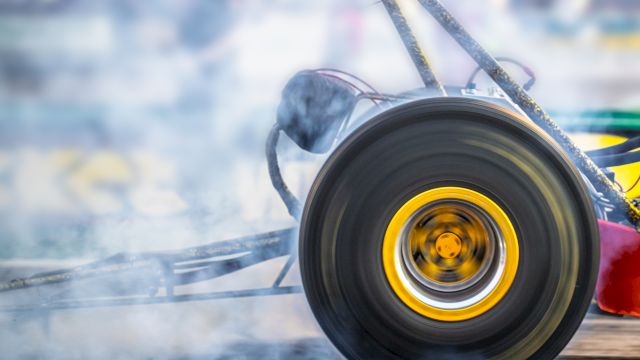 A close-up of a drag racing car's wheel, spinning and emitting smoke during a high-speed race, with a blurred background.