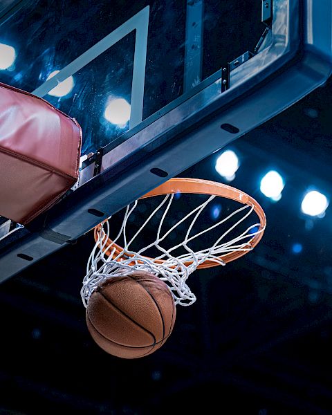 A basketball going through a hoop with a backboard, set against a backdrop of bright arena lights.