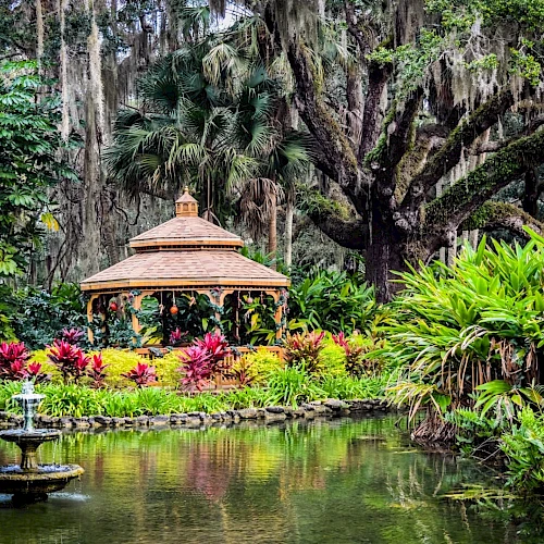 A serene garden scene with a gazebo, surrounded by lush greenery and colorful flowers, reflecting in a pond with a small fountain.