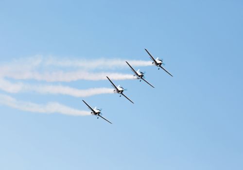 Four airplanes flying in formation with smoke trails against a clear blue sky.