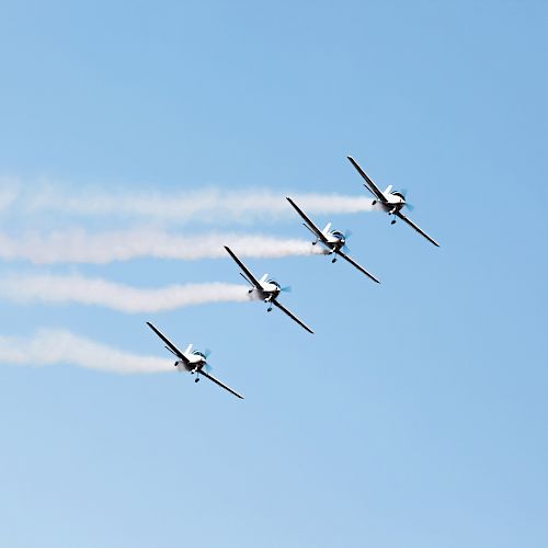 Four airplanes flying in formation with smoke trails against a clear blue sky.