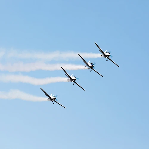 Four airplanes flying in formation with smoke trails against a clear blue sky.