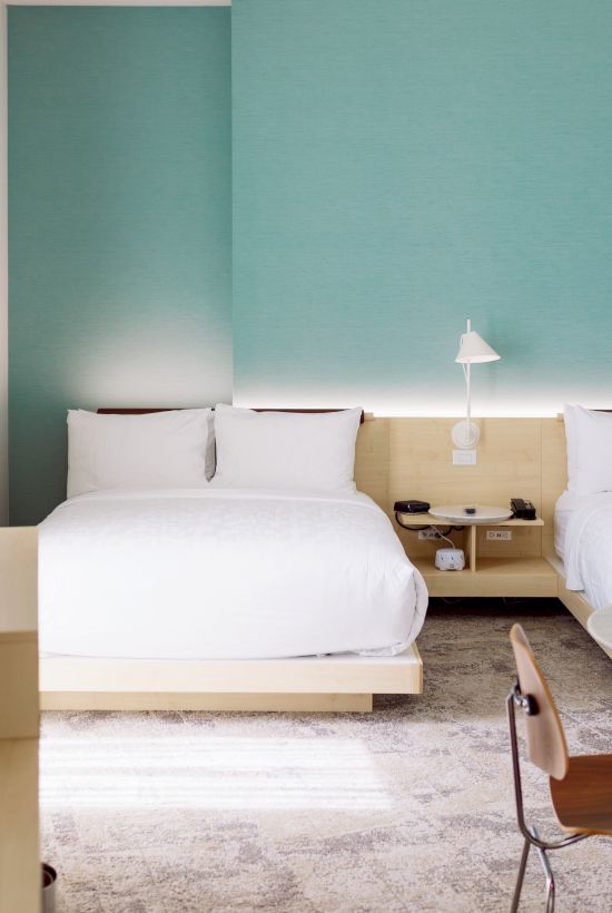 A modern hotel room with two beds, a table and chairs, a flat-screen TV, and a turquoise accent wall.