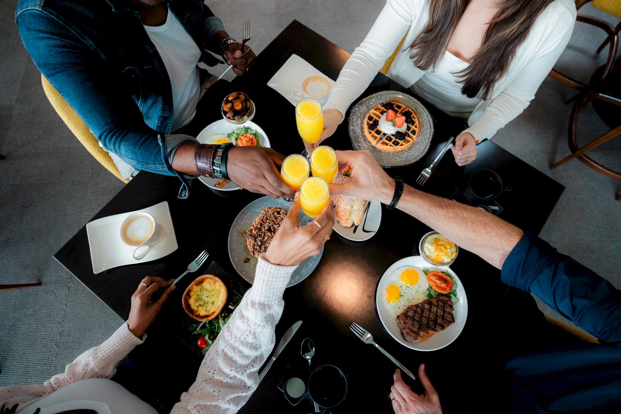 A group of friends cheers with drinks and orange juice, sharing plates of pasta, salads, and desserts around a round table. ending this sentence.