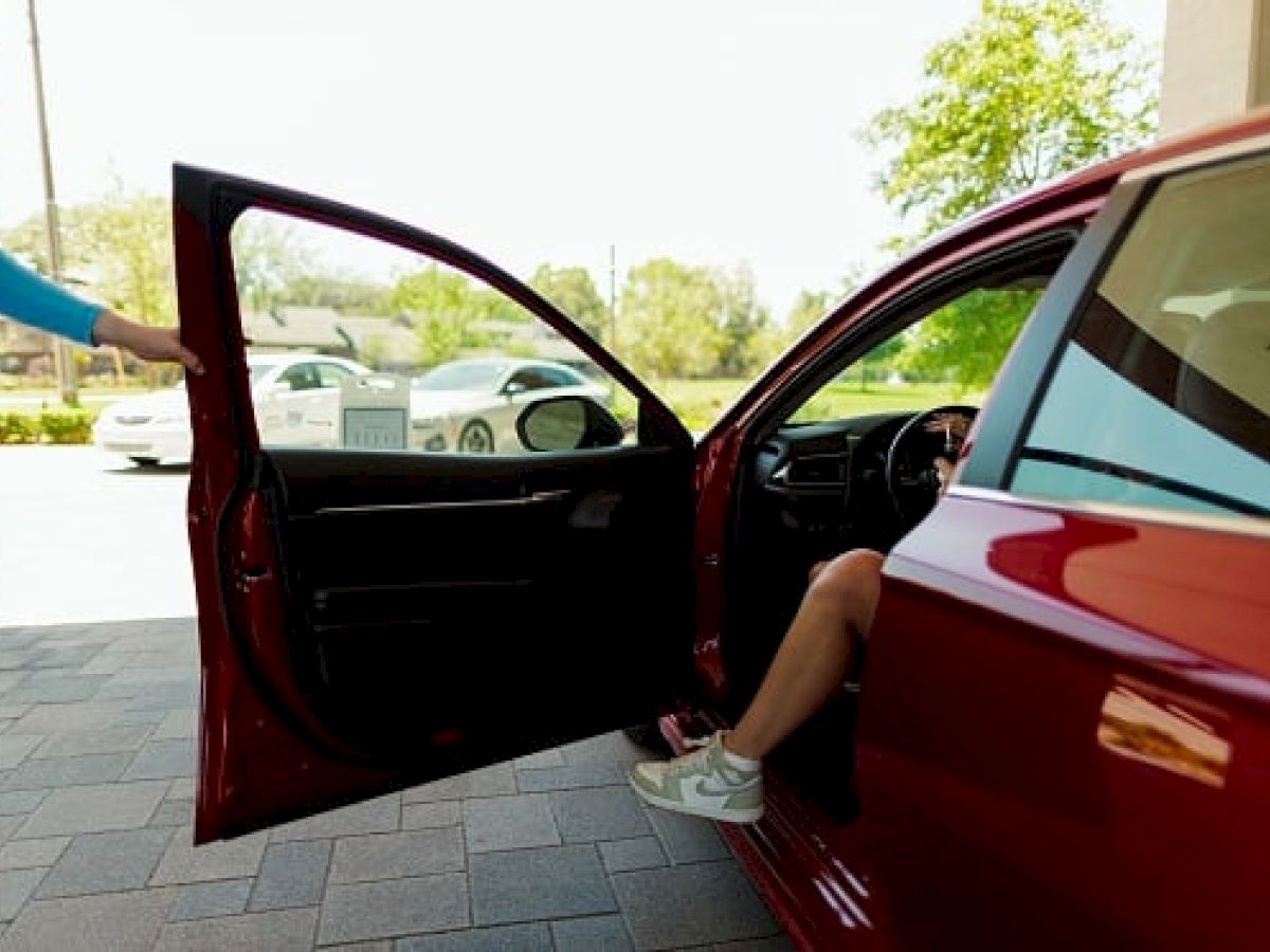 A person is getting into a red car with the driver's door open, while another individual stands nearby.
