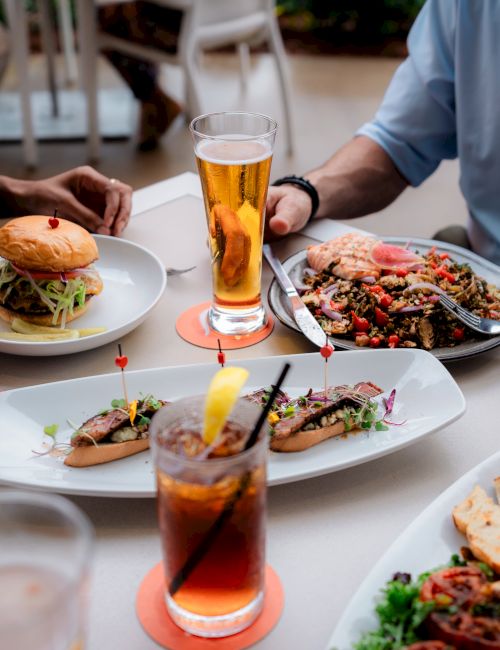 A table with burgers, iced drinks, and a dish of mixed food shared by three people dining together.