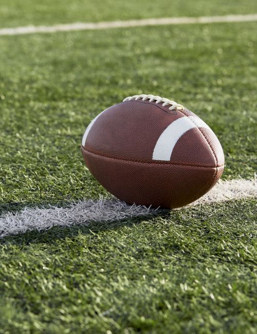 A football is resting on a field with white yard lines visible in the background, suggesting a game or practice environment.