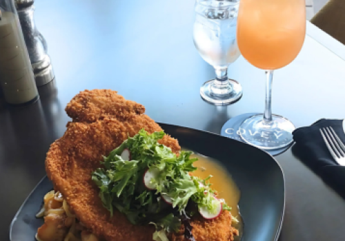 A plate with breaded meat and salad, next to a cocktail garnished with mint and orange.