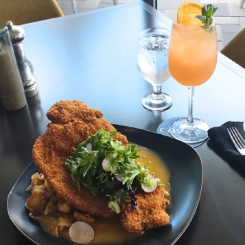 A plate with breaded meat and salad, next to a cocktail garnished with mint and orange.