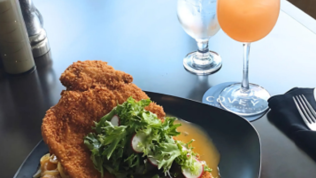 A plate with breaded meat and salad, next to a cocktail garnished with mint and orange.
