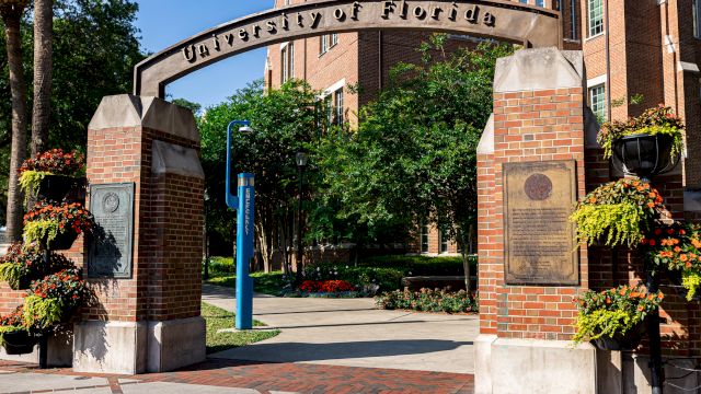 An entrance archway with "University of Florida" inscribed, surrounded by brick pillars and lush greenery in the background.