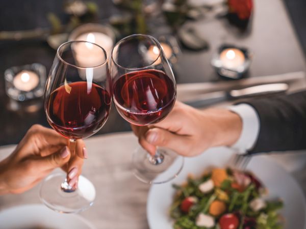 Three people toast with red wine glasses over a plate of salad, set for a classy dinner.