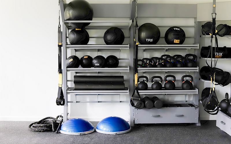 A gym equipment rack filled with TRX medicine balls, kettlebells, dumbbells, and resistance straps for workouts.