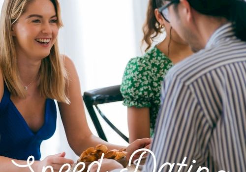 People at a speed-dating singles event, smiling and talking at tables while waiting for partners.