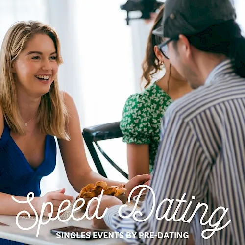 People at a speed-dating singles event, smiling and talking at tables while waiting for partners.